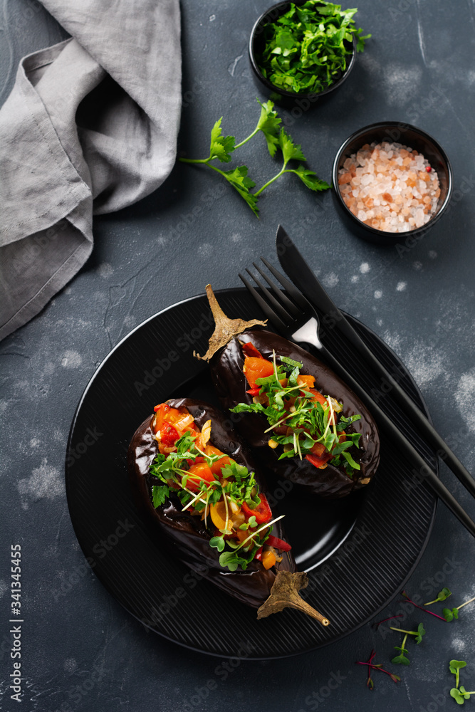 Baked stuffed eggplant with different vegetables, tomato, pepper, onion and parsley on a black stone or concrete table background. Top view.