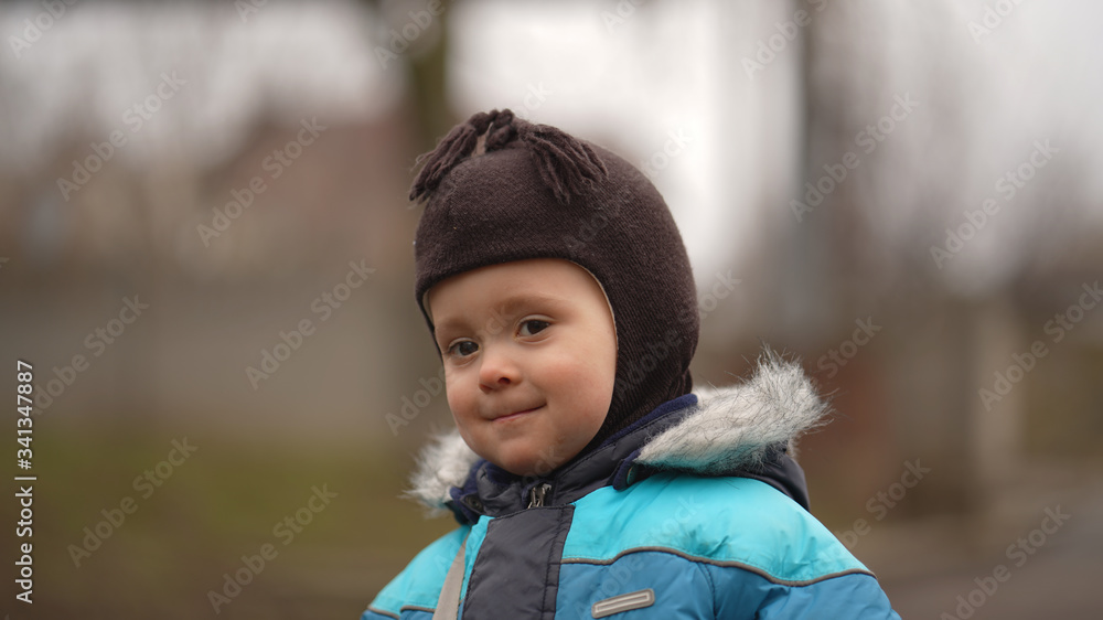 Portrait of little cute boy in blue jacket and brown baby cap in park Portrait of little cute boy in blue jacket and brown baby cap in park