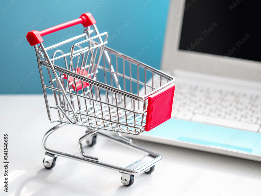 Shopping cart and portable computer. Safe and online shopping on coronavirus quarantine concept. Blue and white background.