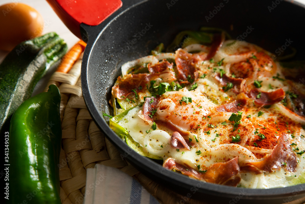 Eggs cooked in a pan with vegetables and iberico ham