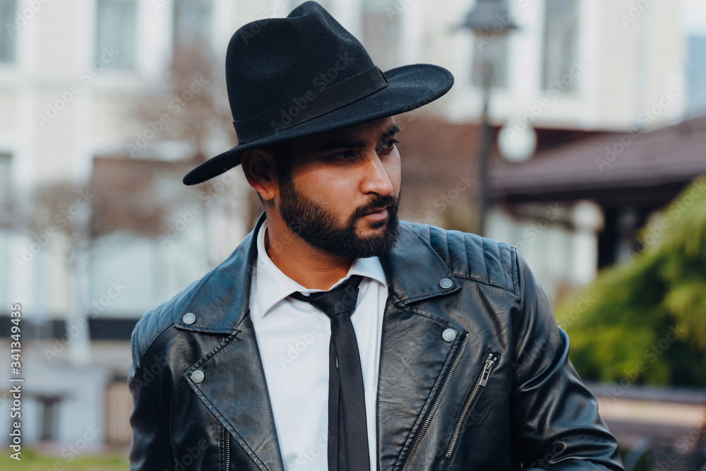 A bearded stylishly dressed Indian man in a black hat walks down the street. A bearded stylishly dressed Indian man in a black hat walks down the street.