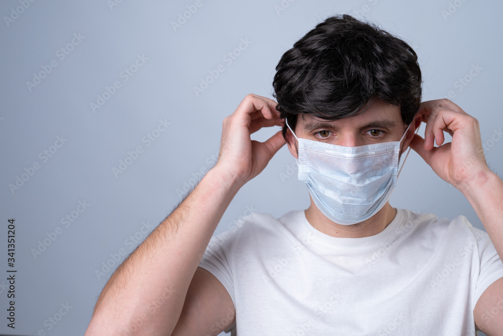 Man puts a medical mask on her face on a gray background