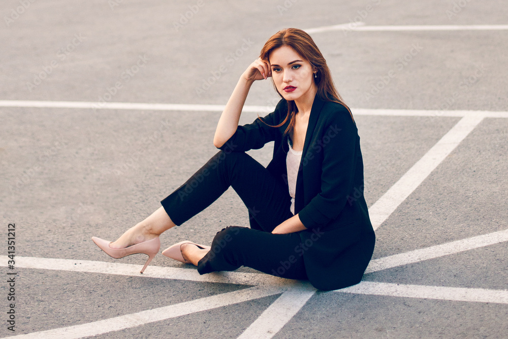Red-haired model in a suit sits in a parking lot in summer Red-haired model in a suit sits in a parking lot in summer