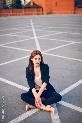 Red-haired model in a suit sits in a parking lot in summer