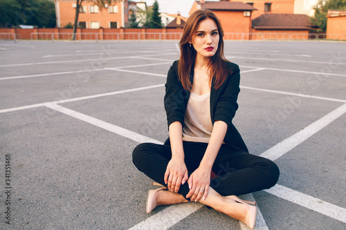 Red-haired model in a suit sits in a parking lot in summer