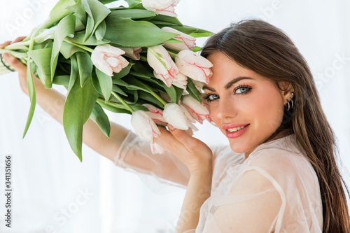 Portrait of cheerful pretty woman in white dress holding bunch of flowers