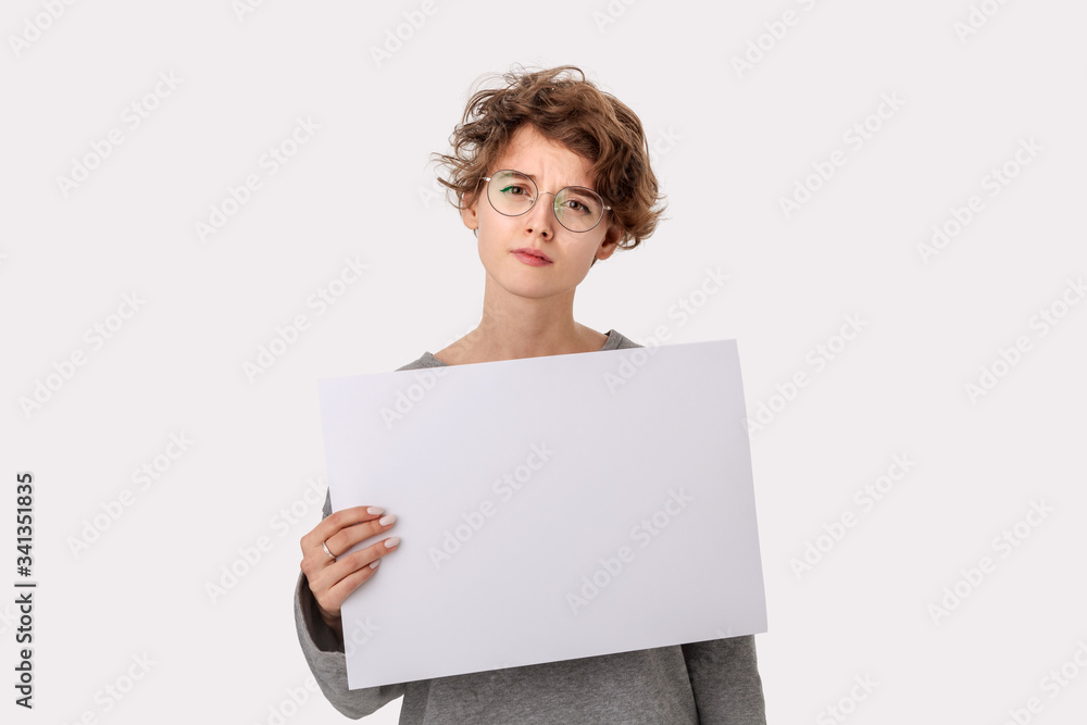 Concerned young woman with eyeglass holding empty blank paper board with copy space Concerned young woman with eyeglass holding empty blank paper board with copy space