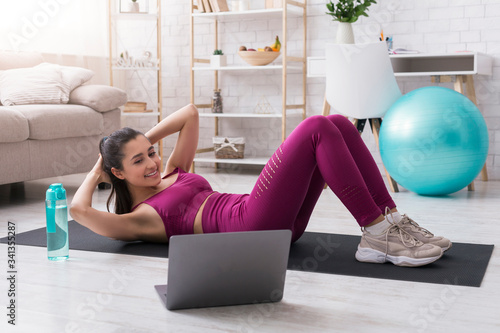 Lockdown sports. Sporty girl doing abs exercises to online workout video at home photo
