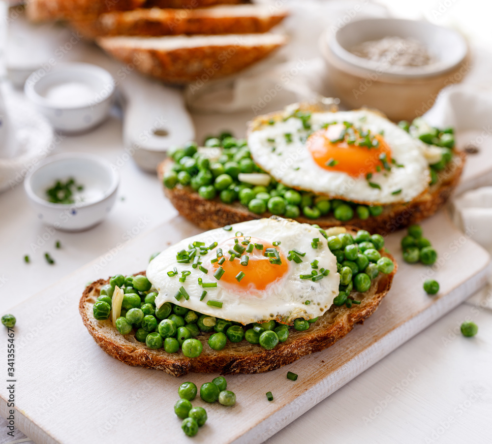 Vegetarian sandwiches made of sourdough bread with the addition of fried egg and stewed green peas on a white board