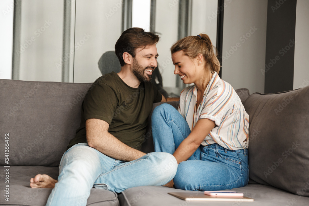 Photo of cheerful couple laughing and talking while sitting on sofa Photo of cheerful couple laughing and talking while sitting on sofa