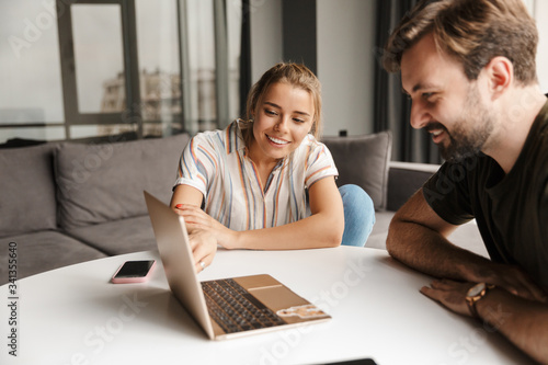 Foto Photo of young joyful couple using laptop and smiling while sitting