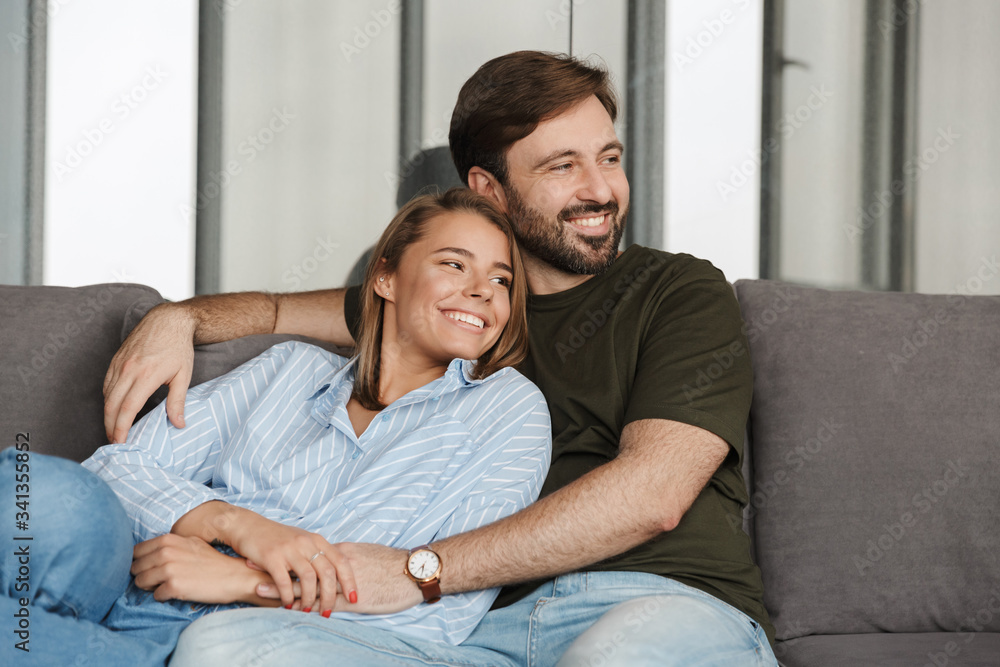 Photo of cheerful couple smiling and hugging while sitting on sofa