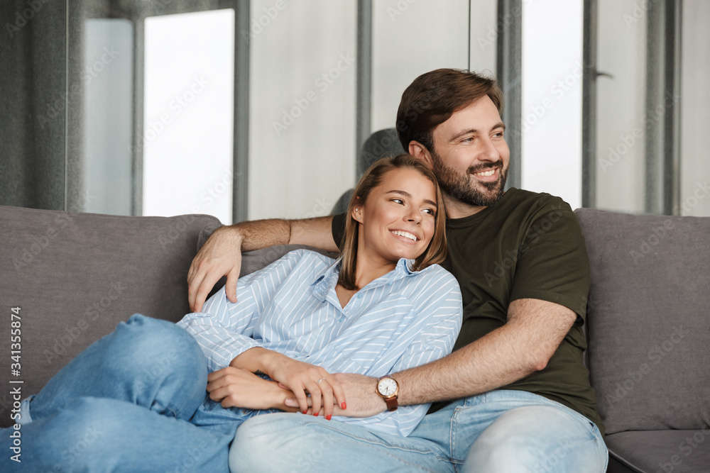 Photo of cheerful couple smiling and hugging while sitting on sofa Photo of cheerful couple smiling and hugging while sitting on sofa