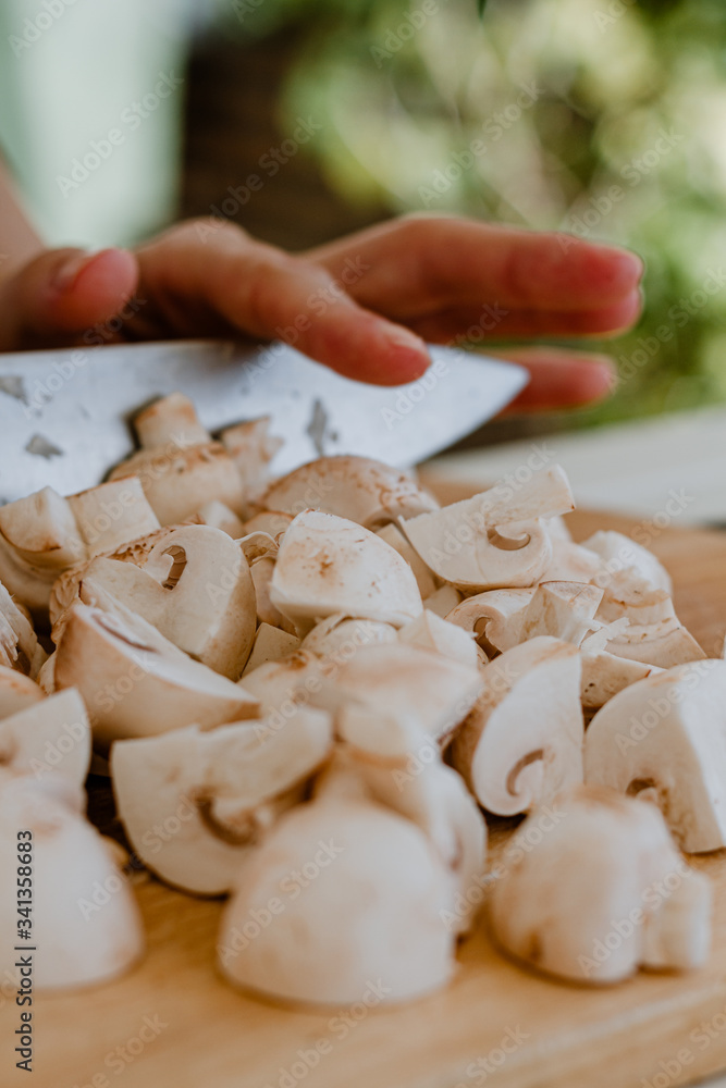 Hands cutting mushrooms with a knife on a wooden board