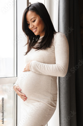 Photo of happy pregnant asian woman smiling and touching her belly