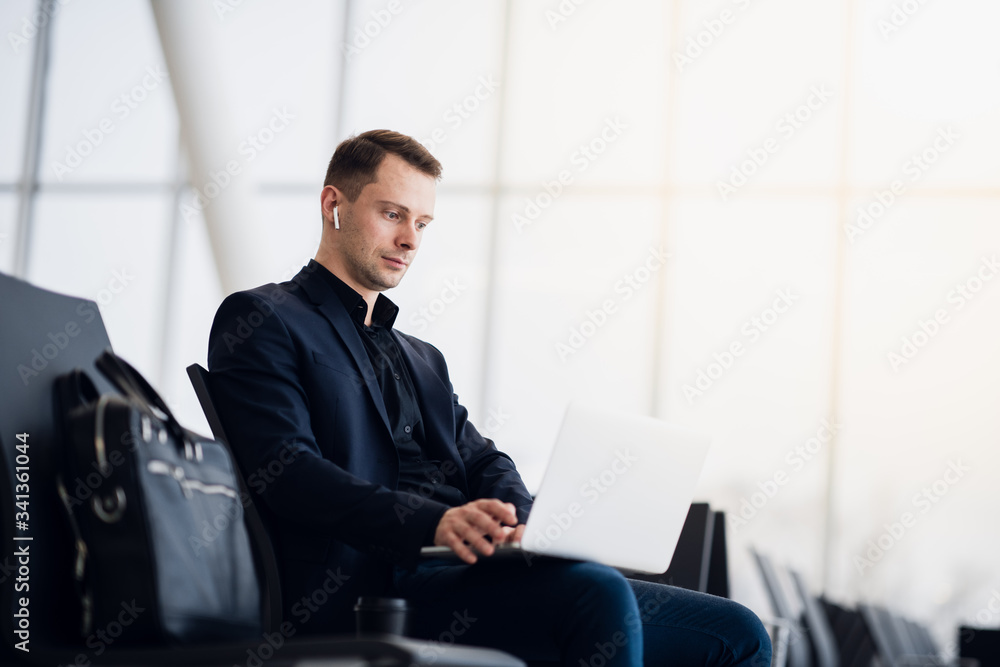 Man with suitcase sitting in airport waiting area while listening music using airpods Man with suitcase sitting in airport waiting area while listening music using airpods