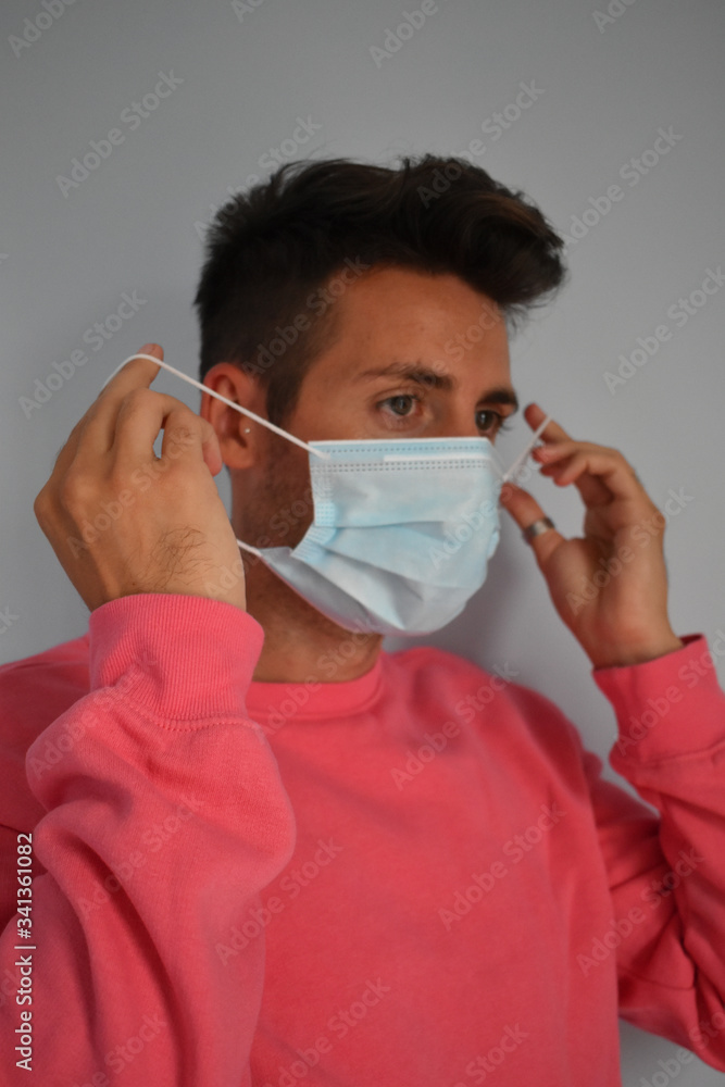Young man in quarantine putting on a surgical mask to protect himself from the coronavirus Young man in quarantine putting on a surgical mask to protect himself from the coronavirus