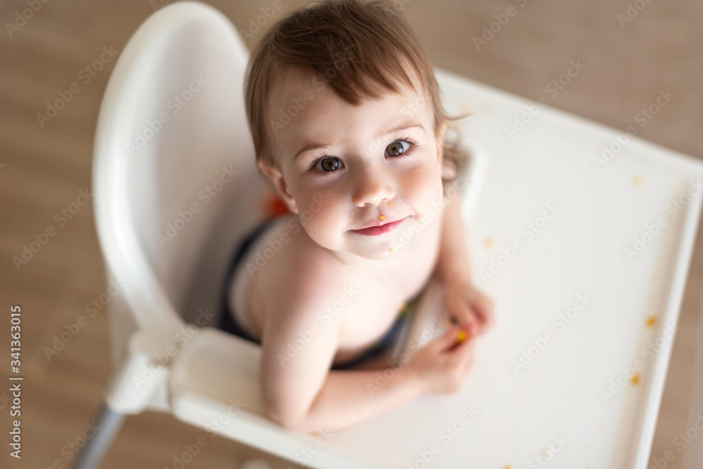 Baby sitting in a highchair and smiling, the face is a bit dirty with food Baby sitting in a highchair and smiling, the face is a bit dirty with food