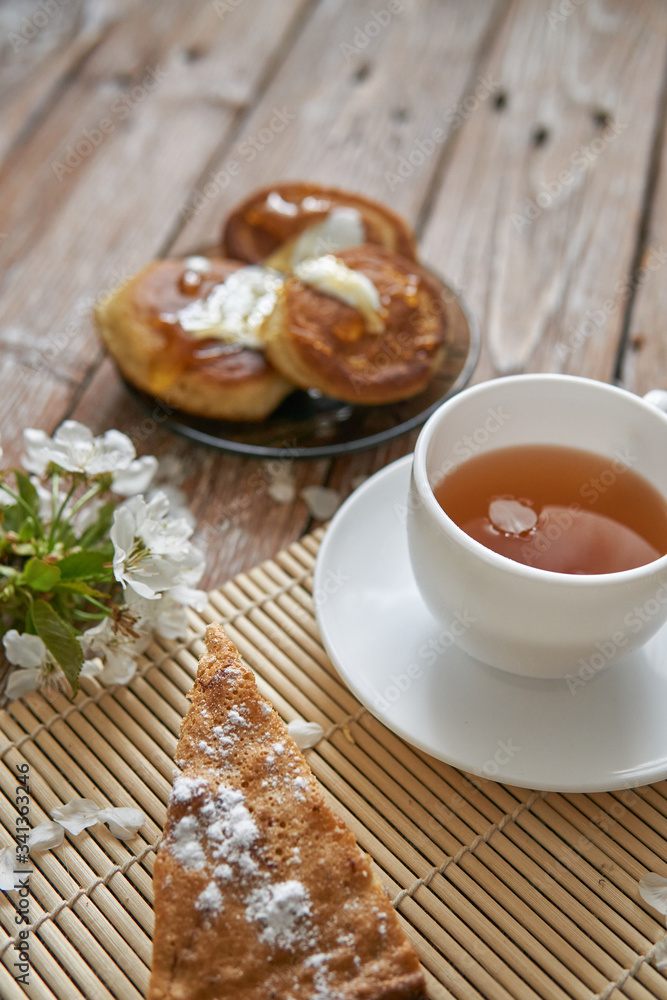 Pile of small homemade pancakes with honey, tea cup and honeycomb on wooden table Pile of small homemade pancakes with honey, tea cup and honeycomb on wooden table