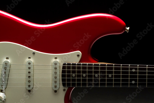 A vibrant red electric guitar over a black background. photo