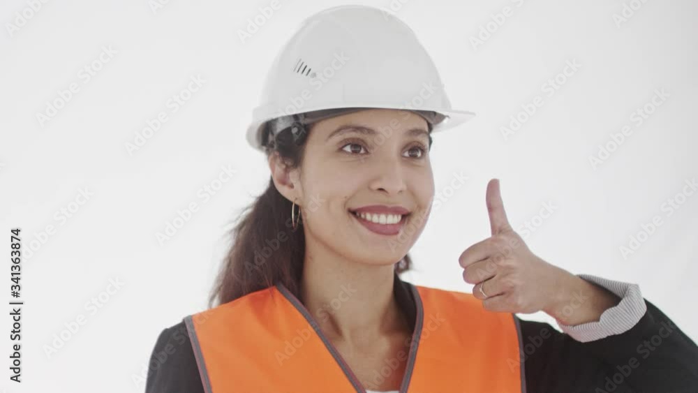 Young satisfied dark-haired woman supervisor in safety equipment smiles broadly and gives thumbs up with both hands. 360 degree tracking arc shot in 4K. Young satisfied dark-haired woman supervisor in safety equipment smiles broadly and gives thumbs up with both hands. 360 degree tracking arc shot in 4K.