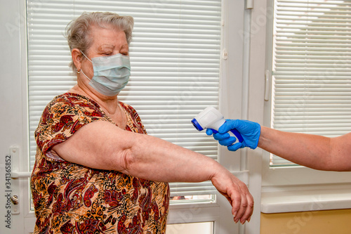 A doctor in blue latex gloves measures the body temperature with an infrared emitter in a woman aged. photo