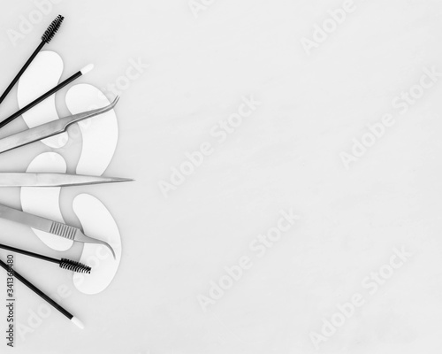 A beauty background design with eyelash extension tweezers, gel eye pads, applicators and mascara wands laid out on the left side of the frame against a white background space for copy text