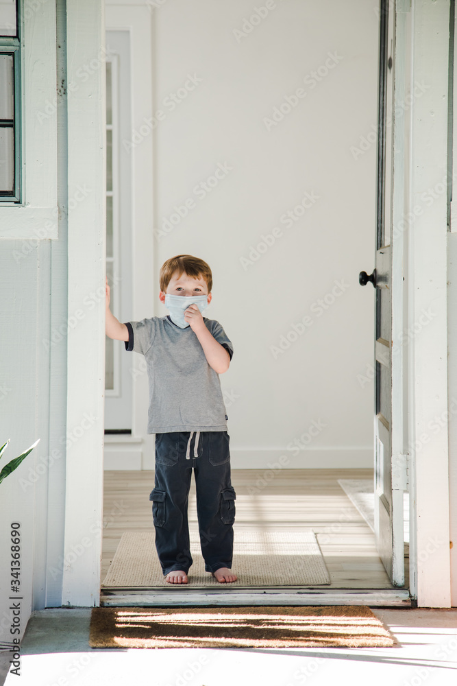 Young Caucasian Boy Standing in Doorway of a House Wearing a Medical Mask Looking at Camera Young Caucasian Boy Standing in Doorway of a House Wearing a Medical Mask Looking at Camera