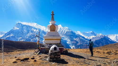 A man standing next to a stupa with snow caped Annapurna chain in the back, Annapurna Circuit Trek, Himalayas, Nepal. High mountains around. Some prayer's flag next to it. Serenity and calmness. photo