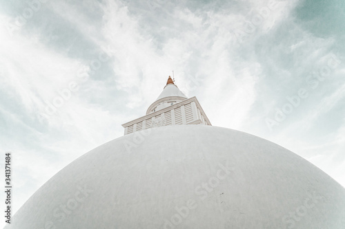 Biała buddyjska świątynia stupa na tle pochmurnego nieba.