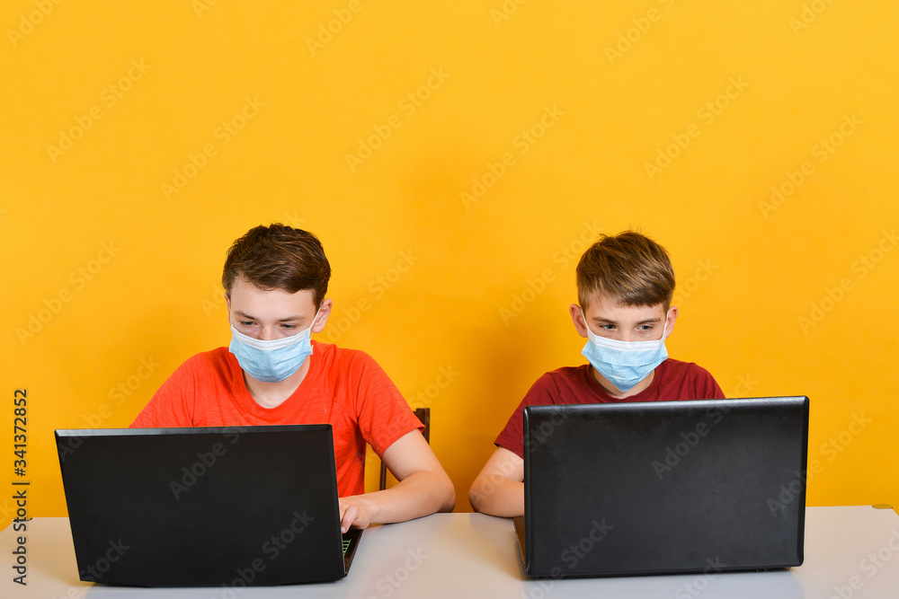 Boys in medical masks are on distance learning and are sitting in front of a laptop monitor, due to the threat of a coronavirus pandemic. Boys in medical masks are on distance learning and are sitting in front of a laptop monitor, due to the threat of a coronavirus pandemic.