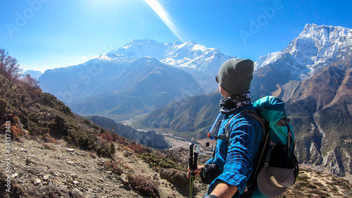 Man taking a selfie while trekking on the Annapurna Circuit Trek, Himalayas, Nepal. Snow caped Annapurna chain in the back. Lots of dried grass. High altitude, massive mountains. Freedom and adventure