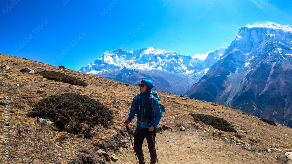 A man trekking on the Annapurna Circuit Trek, Himalayas, Nepal. Panoramic view on snow caped Annapurna chain. Lots of dried grass. High altitude, massive mountains. Freedom and adventure