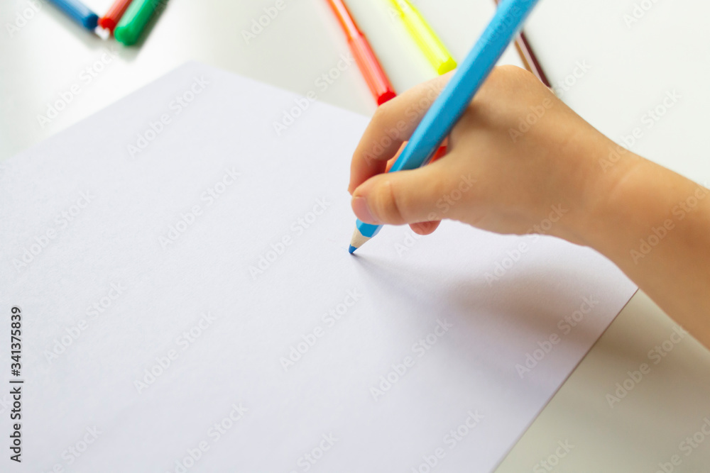 Close up of child's hands drawing at blank white paper with a blue pencil, school background Close up of child's hands drawing at blank white paper with a blue pencil, school background