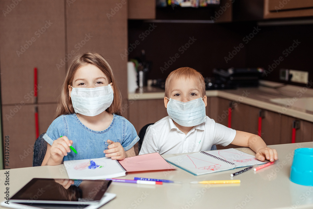 Preschool distance learning at home. two happy children Twins girl and boy in medical masks receive additional education at home using a tablet. They draw in notebooks.
