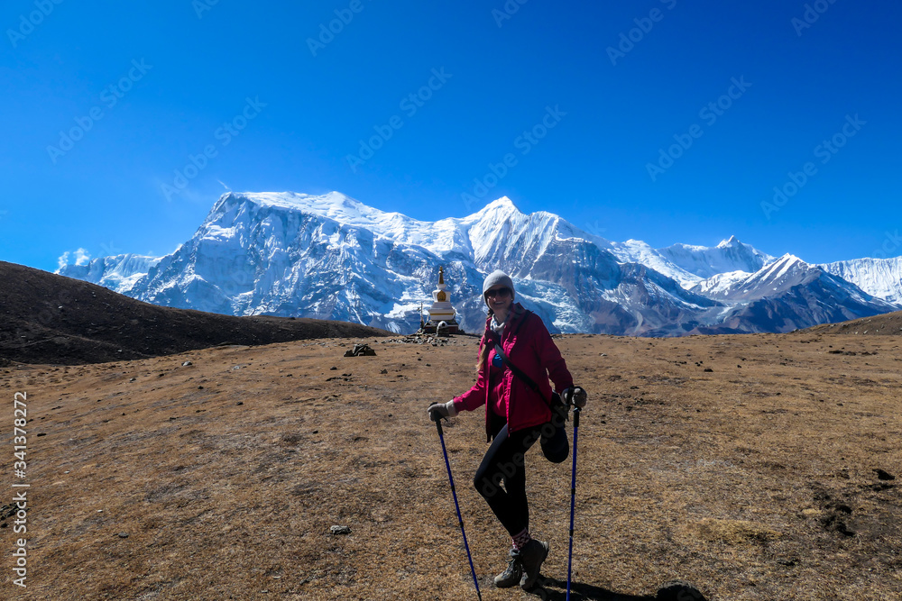 A woman trekking on the Annapurna Circuit Trek, Himalayas, Nepal. Panoramic view on snow caped Annapurna chain. Lots of dried grass. High altitude, massive mountains. Freedom and adventure