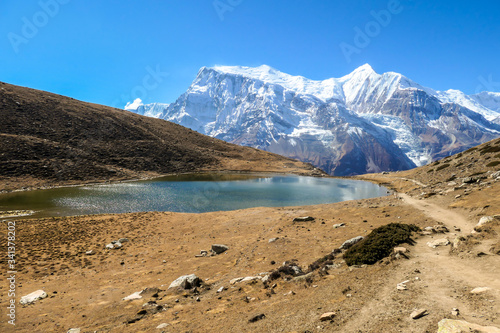 Ice lake, as part of the Annapurna Circuit Trek detour, Himalayas, Nepal. Annapurna chain in the back, covered with snow. Clear weather, dry grass, snowy peaks. Freedom, solitude, chill and relaxation