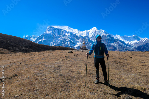 A man trekking on the Annapurna Circuit Trek, Himalayas, Nepal. Panoramic view on snow caped Annapurna chain. Lots of dried grass. High altitude, massive mountains. Freedom and adventure