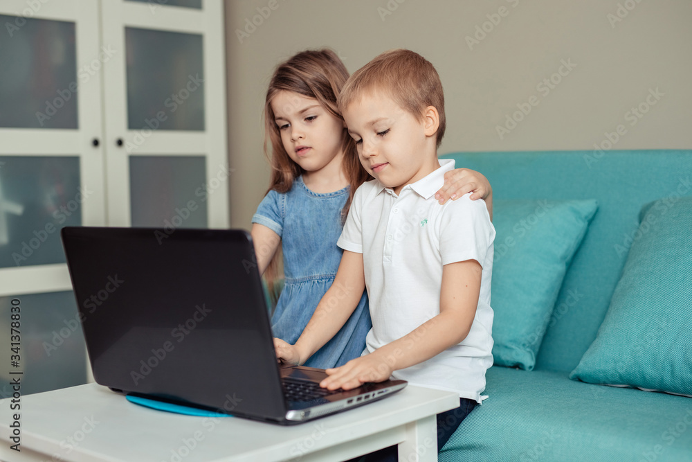 home-based distance education of children during quarantine. happy cheerful twin brother and sister sitting on the couch and doing homework using laptop home-based distance education of children during quarantine. happy cheerful twin brother and sister sitting on the couch and doing homework using laptop