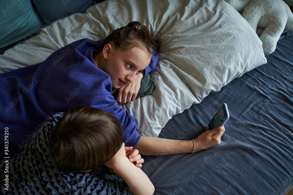 Sibblings lying together on bed using smartphone for video chat Sibblings lying together on bed using smartphone for video chat
