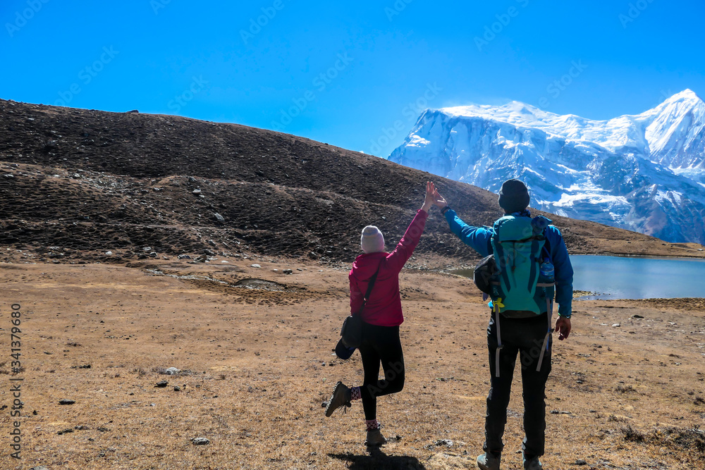 A couple in hiking outfits holding their hands up with the view on Ice Lake, Annapurna Circuit Trek, Himalayas, Nepal. High, snow caped Annapurna chain in the back. Happiness and love