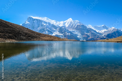 A close up on the Ice lake, along the Annapurna Circuit Trek in Himalayas, Nepal. Annapurna chain in the back, covered with snow. Clear weather, dry grass. Freedom, solitude, chill and relaxation