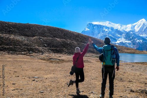 A couple in hiking outfits holding their hands up with the view on Ice Lake, Annapurna Circuit Trek, Himalayas, Nepal. High, snow caped Annapurna chain in the back. Happiness and love © Chris