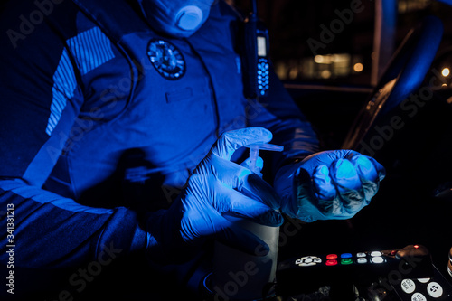 Policeman wearing mask, protective gloves and using sanitizer during emergency mission at night photo