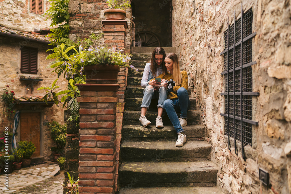 Two young women sitting on stairs looking at smartphone, Greve in Chianti, Tuscany, Italy Two young women sitting on stairs looking at smartphone, Greve in Chianti, Tuscany, Italy