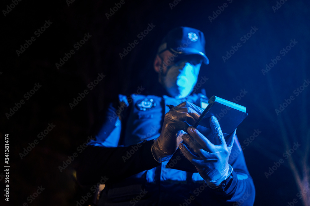 Policeman during emergency mission at night, taking notes, wearing protective gloves and mask Policeman during emergency mission at night, taking notes, wearing protective gloves and mask