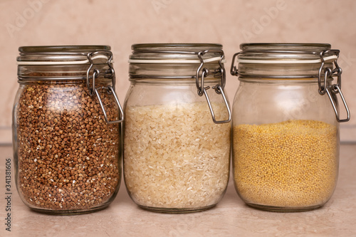 glass jars with buckwheat, wheat groats and rice stand on a wooden table photo