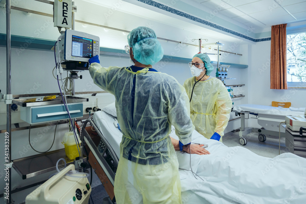Doctors caring for patient in emergency care unit of a hospital looking at screen Doctors caring for patient in emergency care unit of a hospital looking at screen