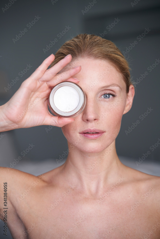 Portrait of beautiful woman holding cream jar in front of her eye Portrait of beautiful woman holding cream jar in front of her eye