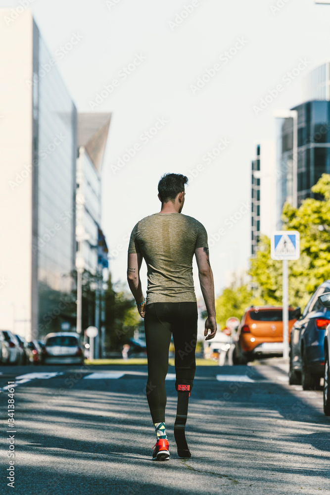 Rear view of disabled athlete with leg prosthesis walking on a street in the city Rear view of disabled athlete with leg prosthesis walking on a street in the city